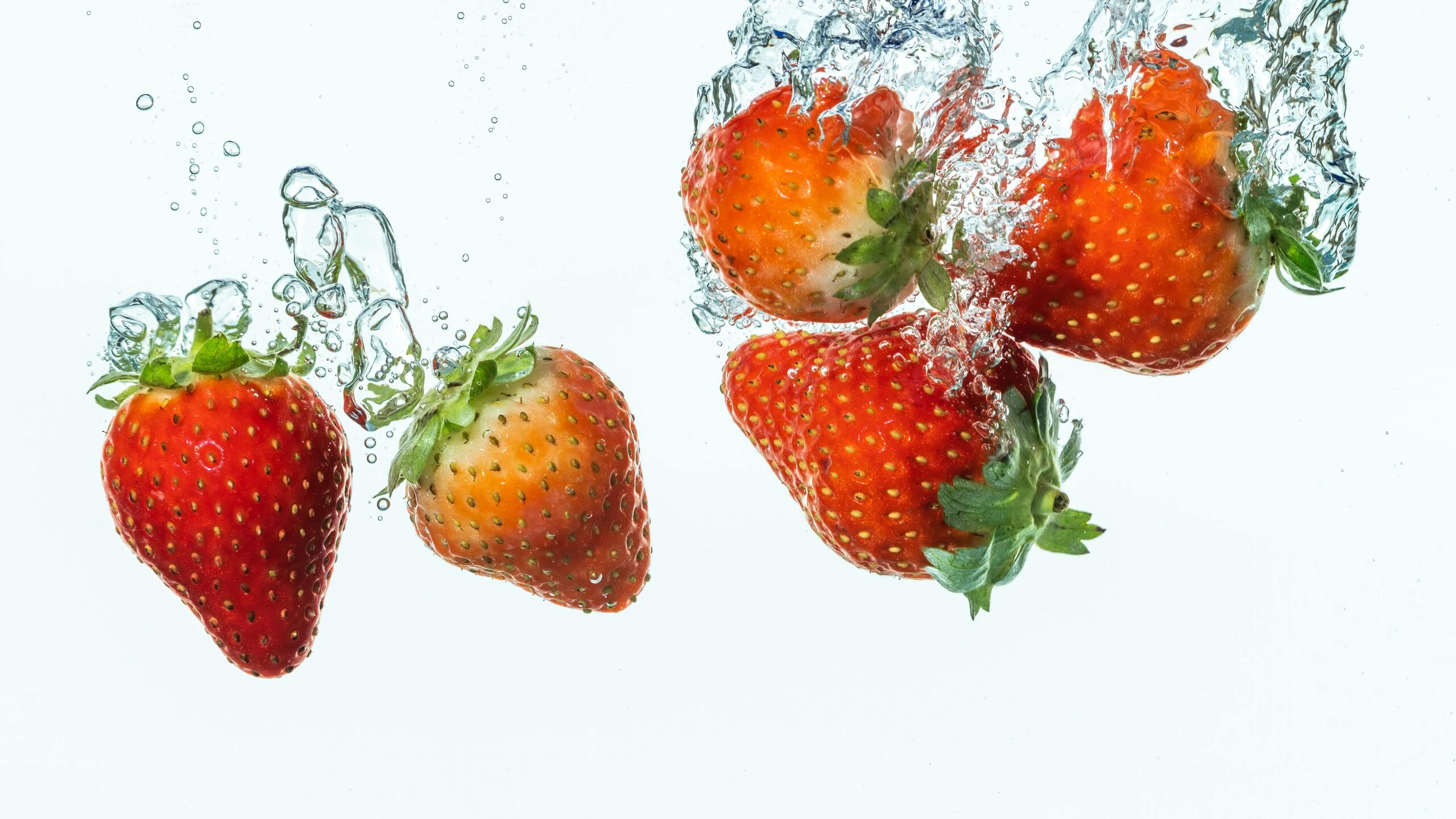 Dynamische Aufnahme von im Wasser planschenden Erdbeeren, die eine energiegeladene Szene schafft.