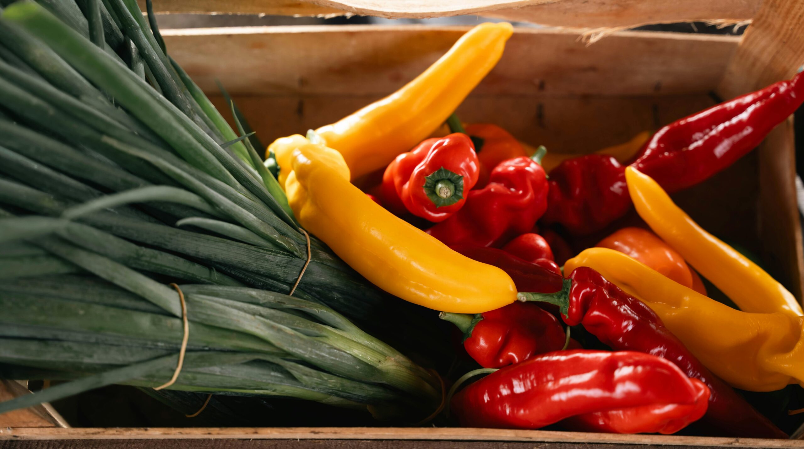 Bunte PrÃ¤sentation frischer Paprika und FrÃ¼hlingszwiebeln in einer rustikalen Holzkiste, ideal fÃ¼r den kulinarischen Gebrauch.